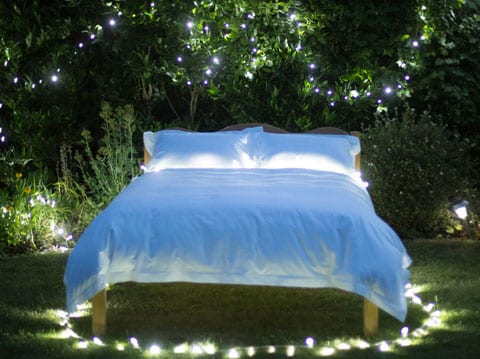 Made bed in garden on warm summers night surrounded by lights scooms