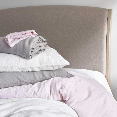 Bundle of grey, white and pink super soft linen on a bed