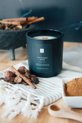 Best fall candles, cinnamon spice wooden wick soy candle sitting on a turkish towel next to a bowl of ground cinnamon, cinnamon sticks and spices.