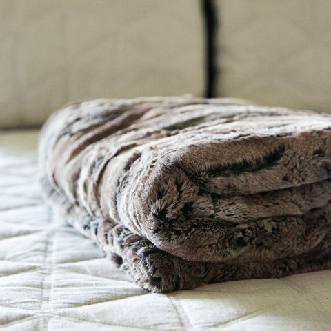 Super soft and comfy faux fur throw blanket folded up on a bed in a master bedroom.