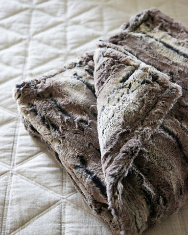 Super soft and comfortable neutral faux fur throw blanket folded on a bed in a master bedroom