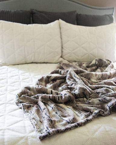 Soft and comfortable faux fur 50x60 standard size throw blanket thrown on a bed in a master bedroom with a white comforter.