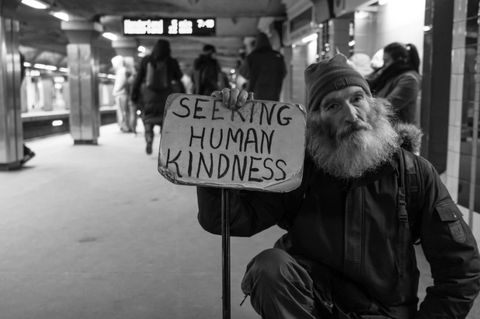 homeless man holding a seeking kindness sign