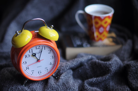 Clock, tea, and a book on a bed