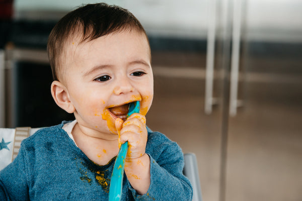 baby boy with spoon in his mouth and food on his face