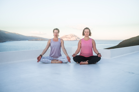 two girls sit in meditation on rooftop by beach