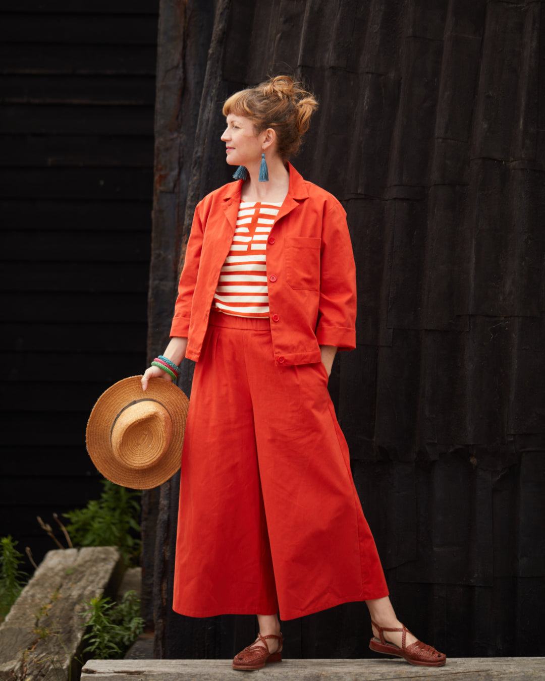 Woman wears a red twin piece - jacket and trousers - with a red and white stripy top. 