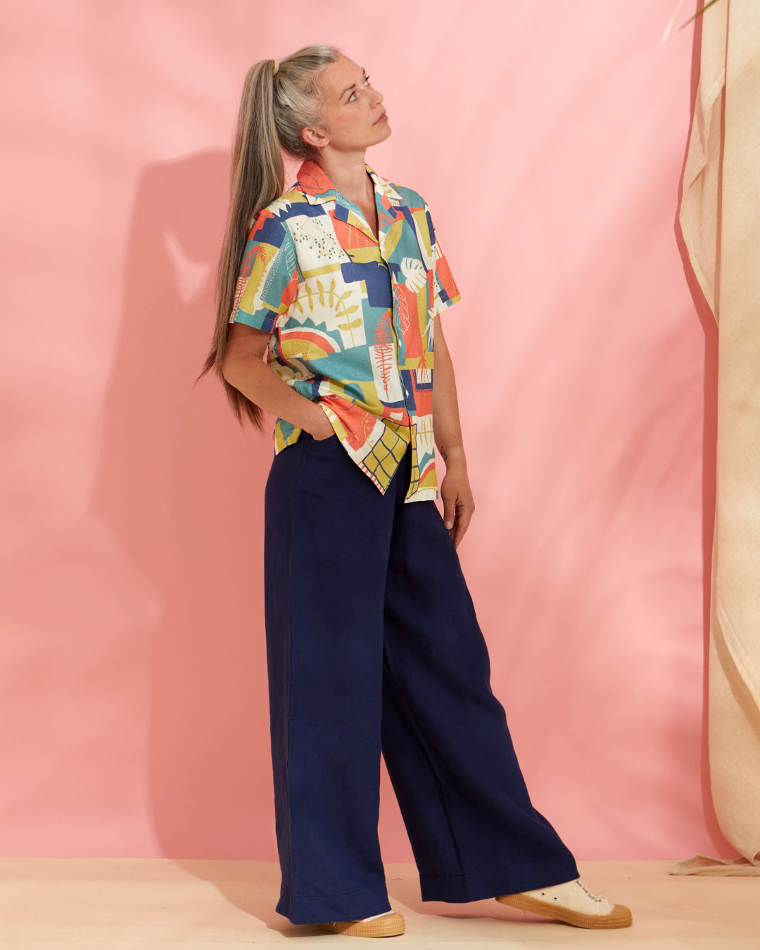 Woman wears a palm leaf printed wrap dress in front of a pink background