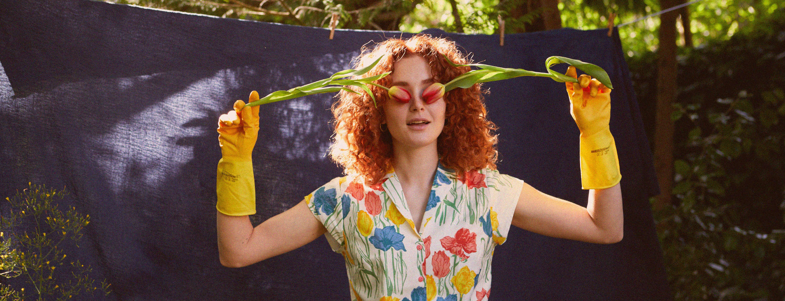 Woman wearing a tulip printed top, holding tulips in front of her eyes