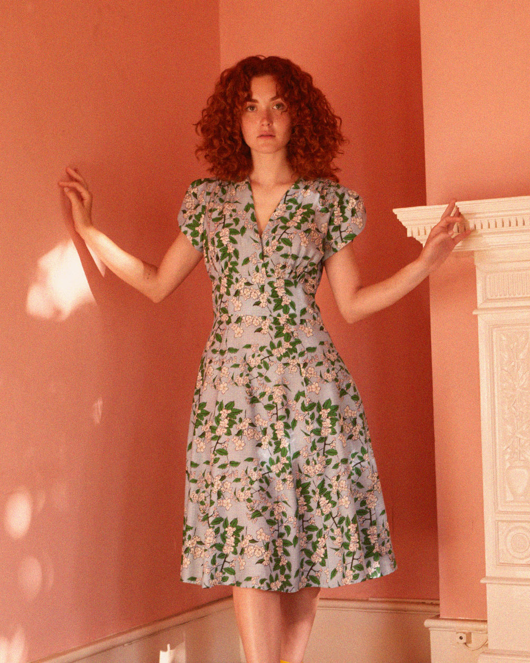 Woman wears a V neck blue dress with white apple blossom flowers printed on it.