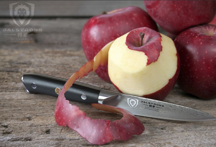 A photo of the Paring Knife 3.5" Shogun Series ELITE Dalstrong with a half peeled apple on top of a wooden table.