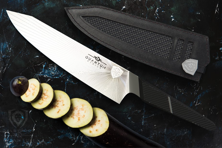 A photo of the Chef's Knife 8.5" Quantum 1 Series | Dalstrong with sheath and sliced egg plant beside it.