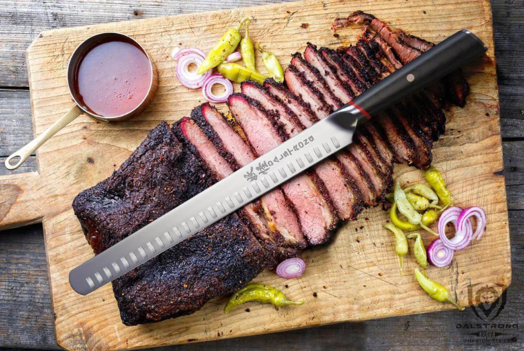 Sliced barbecue brisket on a black surface with a stainless steel slicing knife laying in front