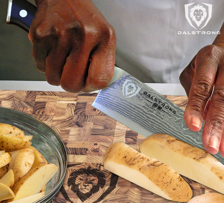 A man slicing raw potatoes with a sharp kitchen knife on a wooden cutting board