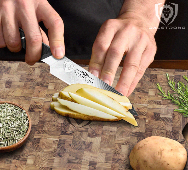 Hands using a paring knife to chop raw potato on a wooden cutting board