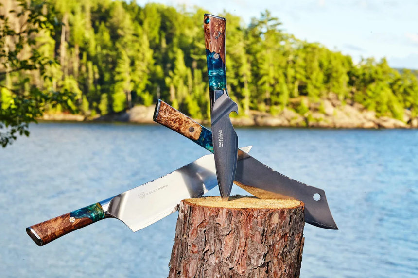 Three Dalstrong Valhalla series knives on top of a log.