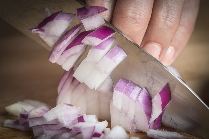 A man's hand chopping an onion.