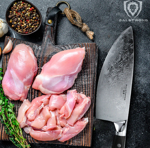 Dalstrong knife beside herbs and spices, and slices of chicken thighs on a wooden cutting board