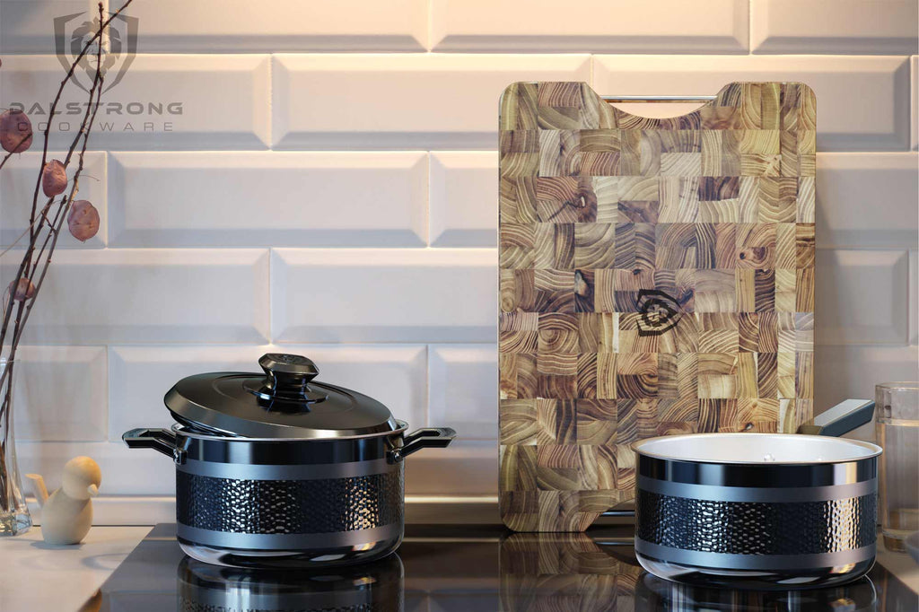 Two black pots on an induction stove top with a wooden cutting board leaning against the background wall