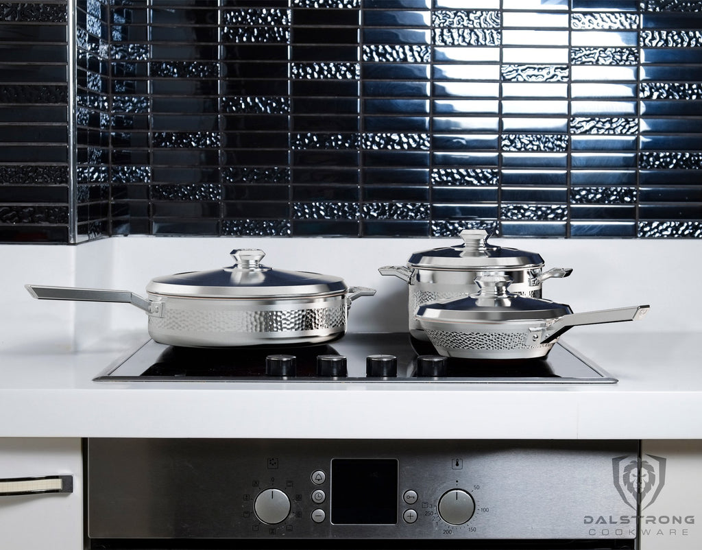 Three silver pieces of cookware on a stove induction top in a white and black kitchen