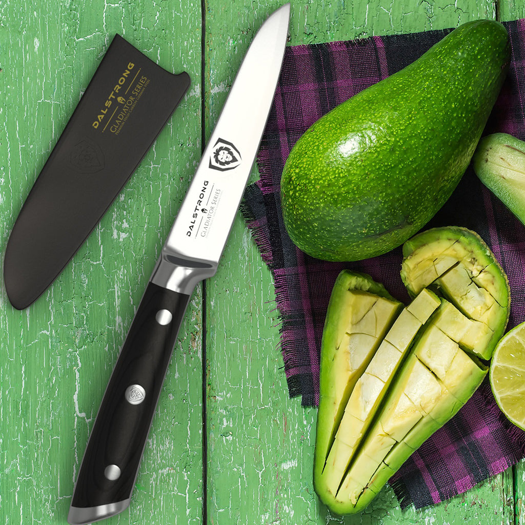 A paring knife and sheath on a green surface next to an avocado chopped in half