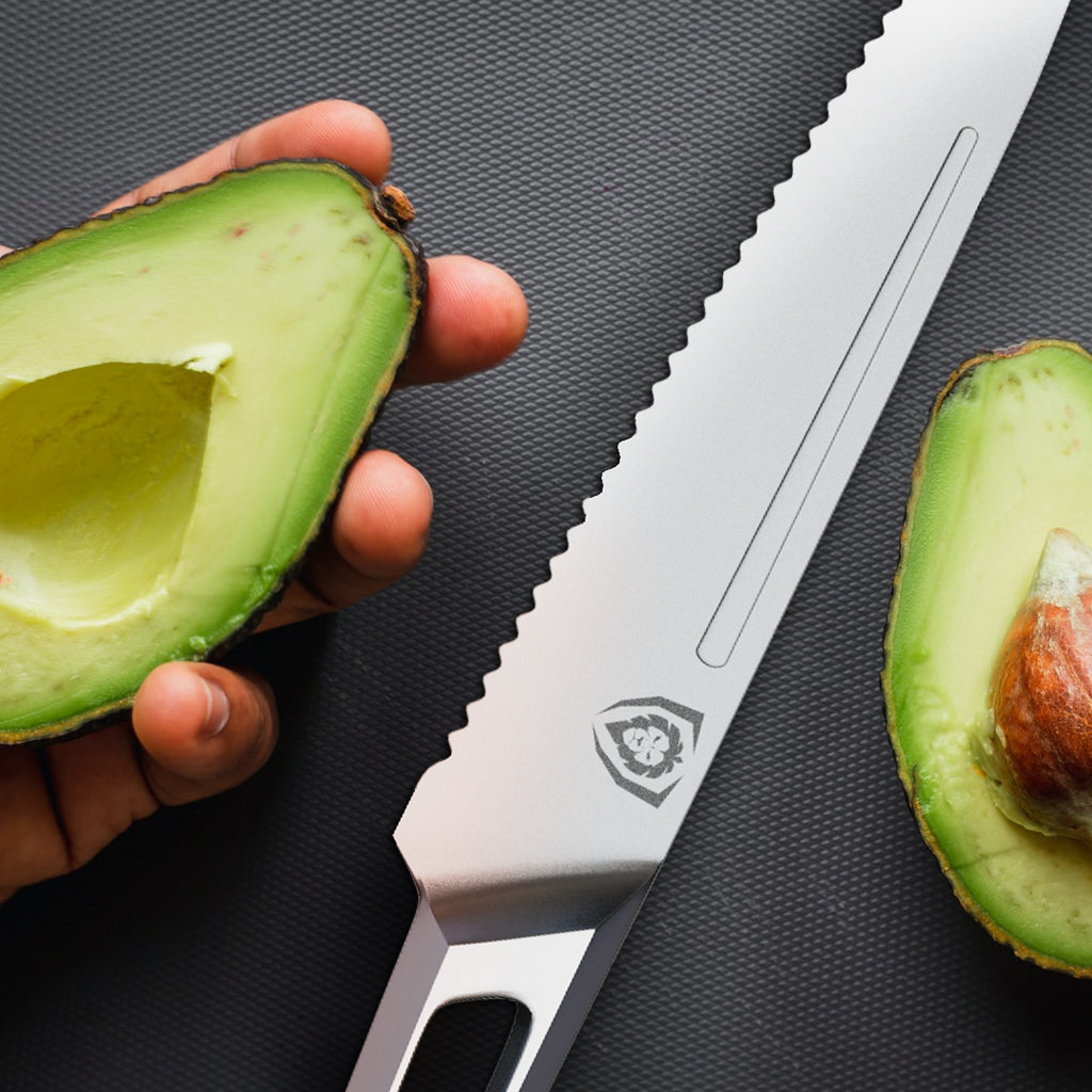 A hand holding an avocado chopped in half next to a stainless steel serrated knife