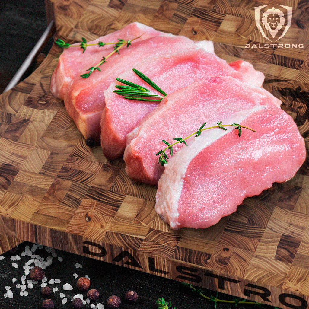 Fresh raw slices of pork chops on a Dalstrong Lionswood Colossal Teak Cutting Board garnished with rosemary on top