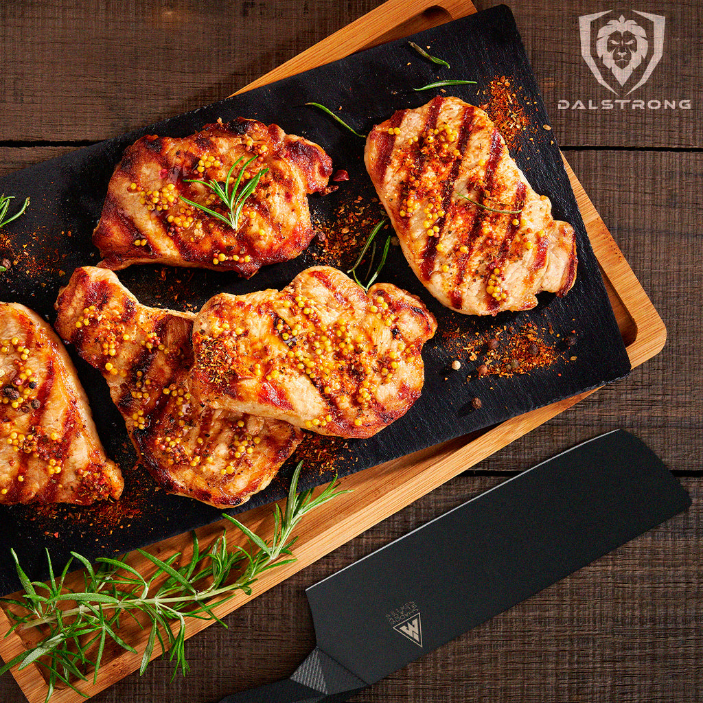 Delicious boneless Pork Chops on a black platter with wooden cutting board underneath and a black knife on the side.