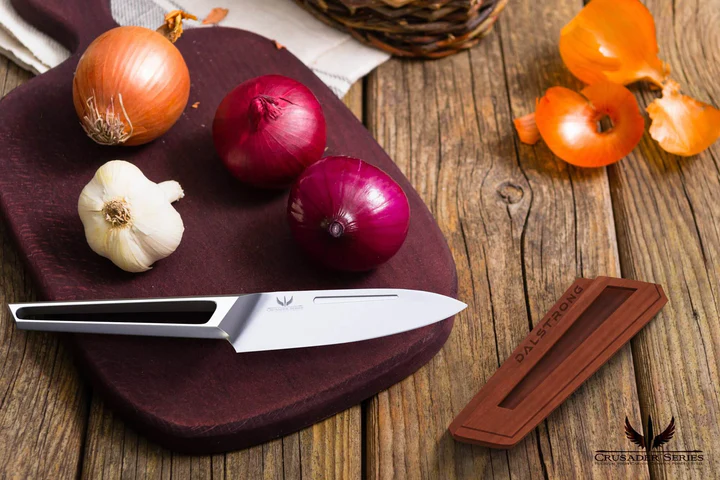 A garlic bulb and thee onions beside the Paring Knife 3.5" Crusader Series | NSF Certified | Dalstrong on top of a chopping board on a wooden table