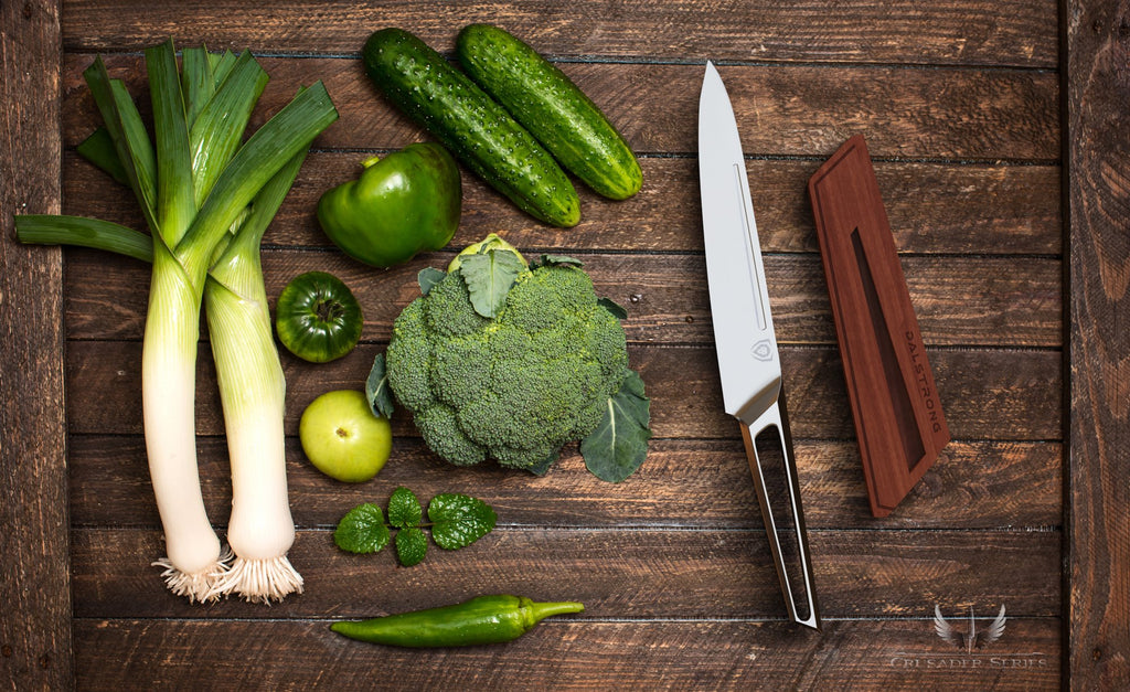 Green vegetables on a wooden surface next to a sharp stainless steel utility knife