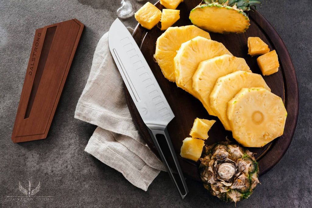 A stainless steel santoku knife beside a cutting board containing chopped pineapple slices