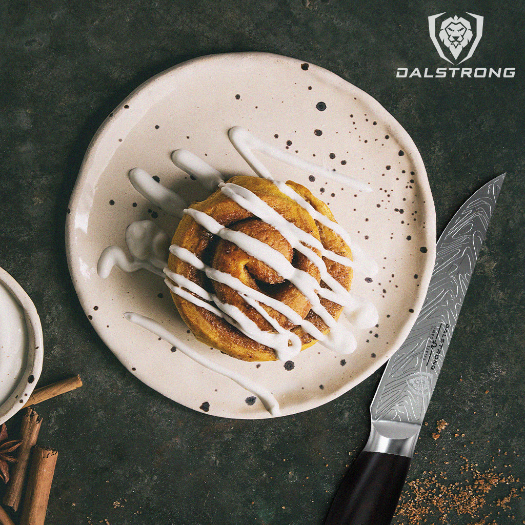 A cinnamon bun with cream cheese on top served on a plate with an Omega Series Paring knife next to it.