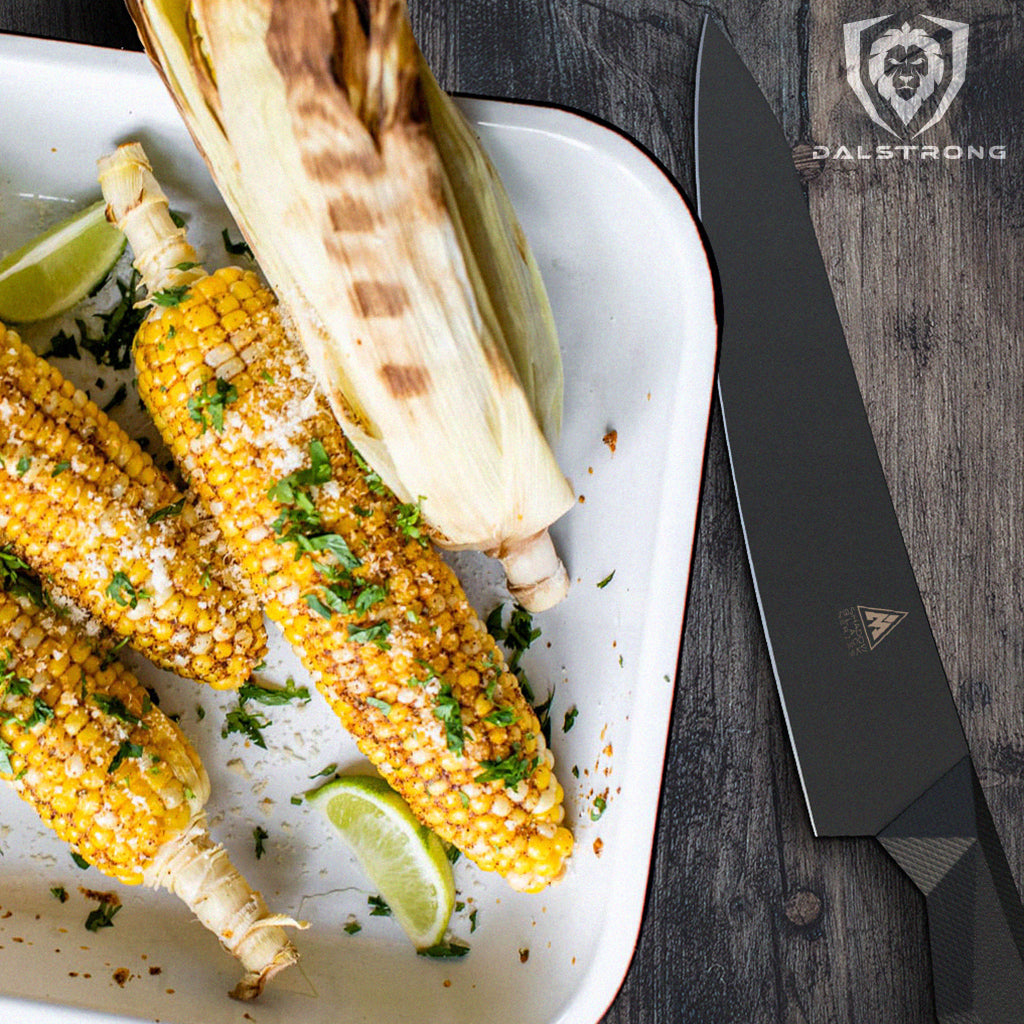A white baking dish of corn on the cob next to a black kitchen knife