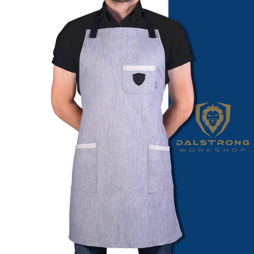 Man standing with his hands behind his back displaying “The Gandalf” grey denim apron with a white and blue background and Dalstrong logo