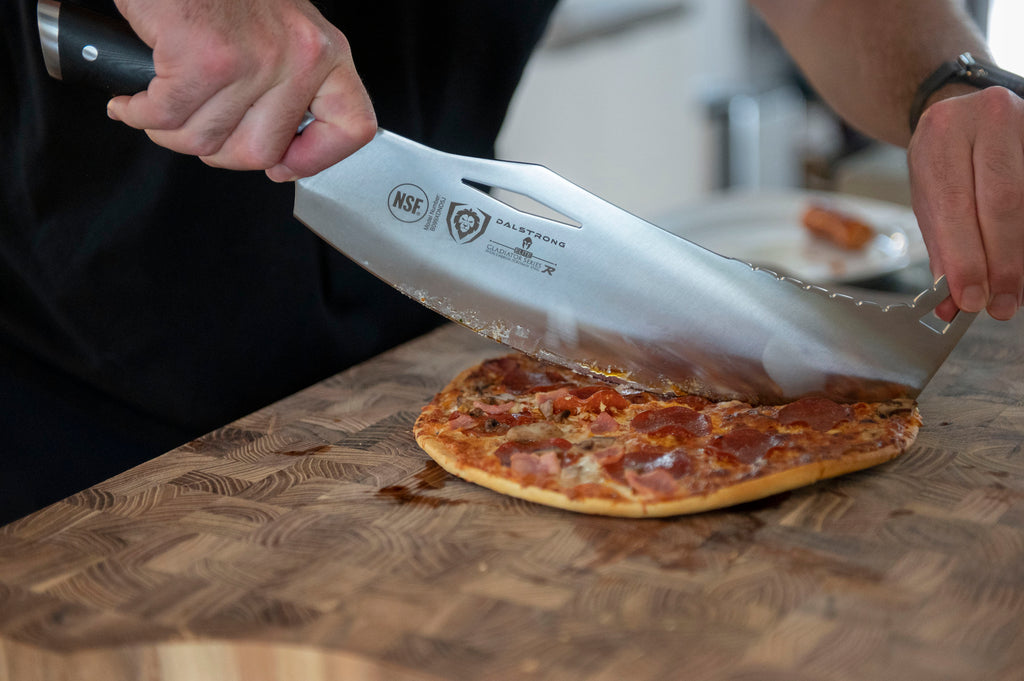 A photo of the Dalstrong 12" Rocking Cleaver Knife slicing a freshly cooked pizza on top of a Dalstrong wooden board.