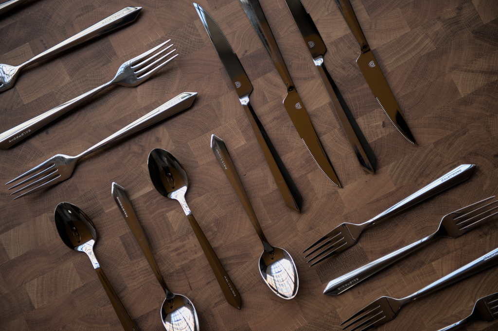 A flat-lay photo of the Dalstrong 20-Piece Flatware Set on a wooden cutting board.