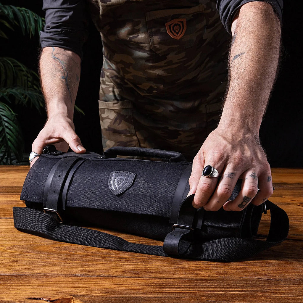 A man holding the 12oz Heavy Duty Canvas & Leather | Nightmaster Black | Nomad Knife Roll | Dalstrong on top of a table.