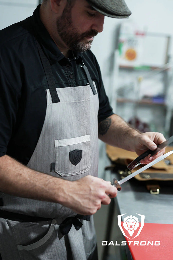 A man wearing the Professional Chef's Kitchen Apron The Gandalf with a honing rod and a knife.
