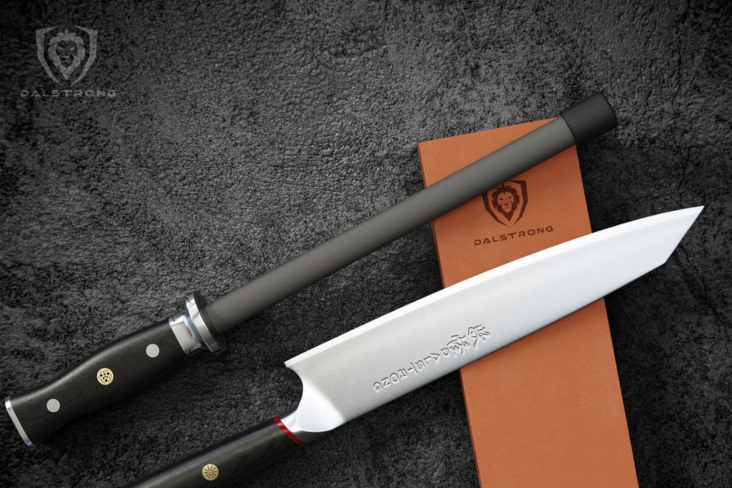 A black ceramic honing steel rests on an orange whetstone next to a chef knife against a black background