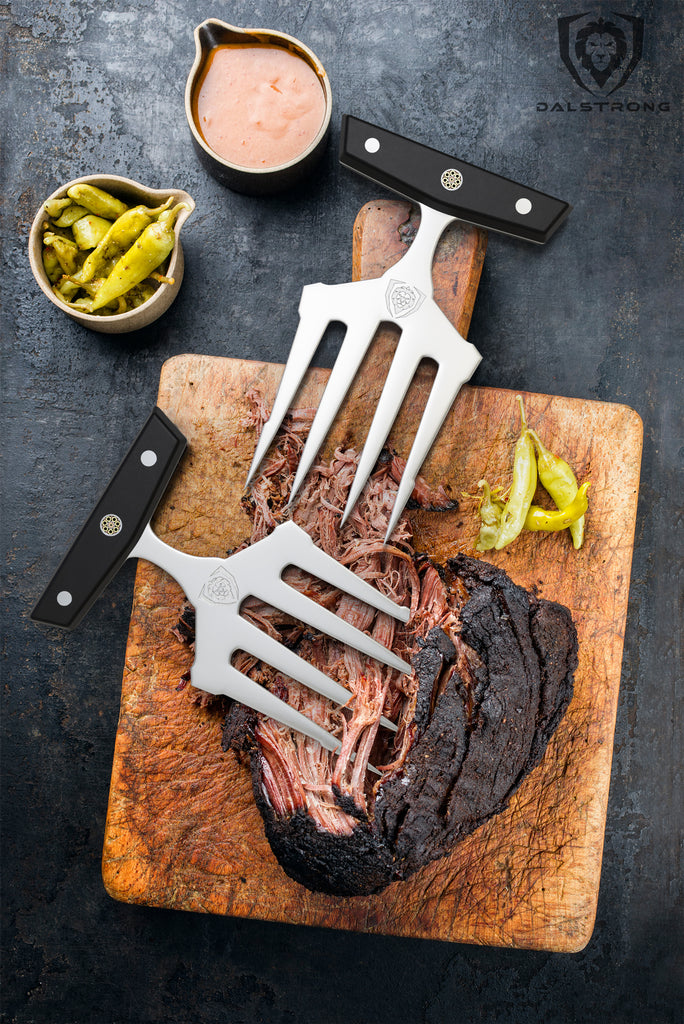 Cooked brisket on a wooden cutting board next to meat shredding claws 