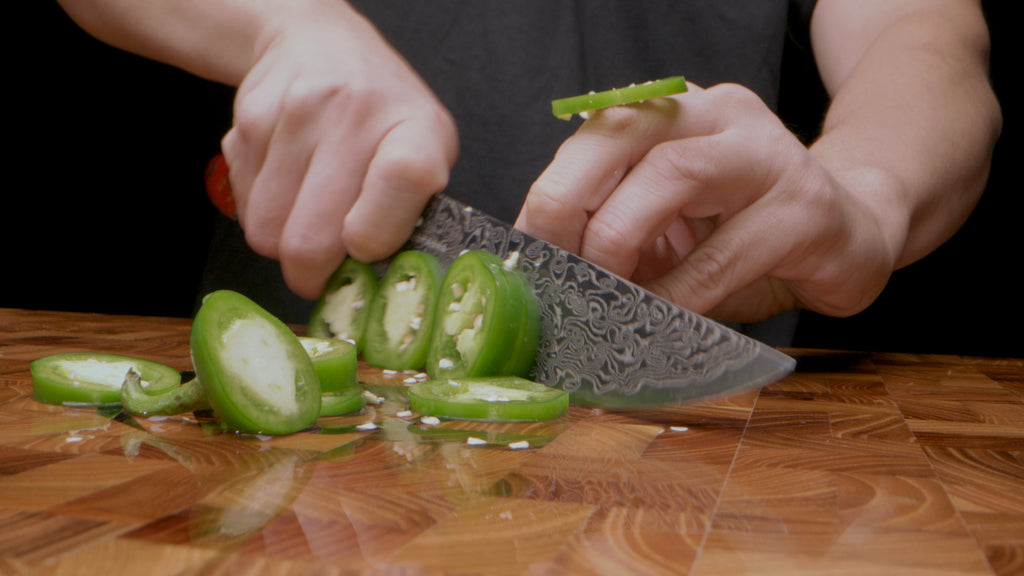 Dalstrong Scorpion Series Chef's Knife slicing jalapenos on a Dalstrong cutting board.