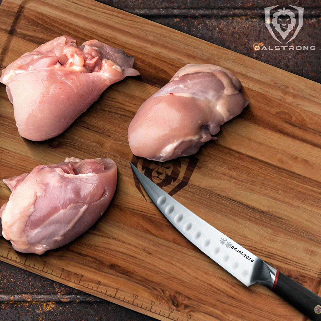 Dalstrong Phantom Series Boning Knife beside three chicken thighs placed on top of a wooden cutting board.