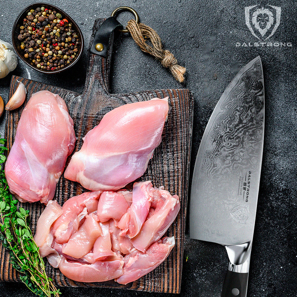 Dalstrong knife beside herbs and spices, and slices of chicken breasts on a wooden cutting board