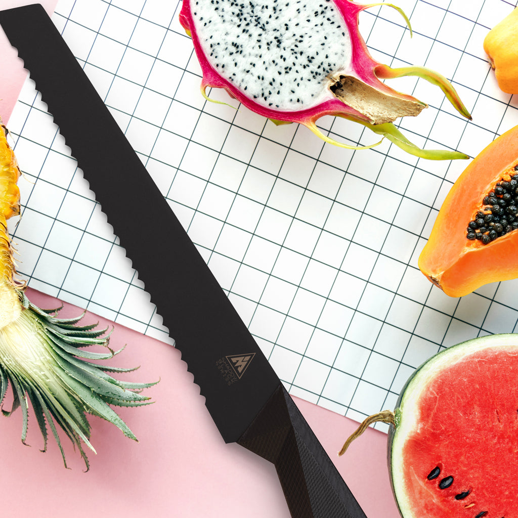 A black bread knife next to chopped fruit including dragon fruit