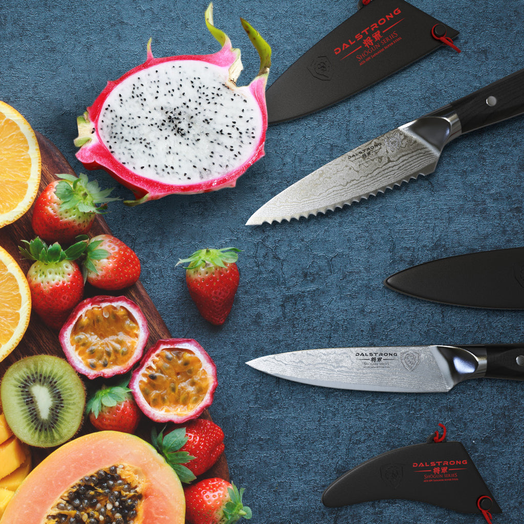 A pile of fruit next to two sharp paring knives against a blue background