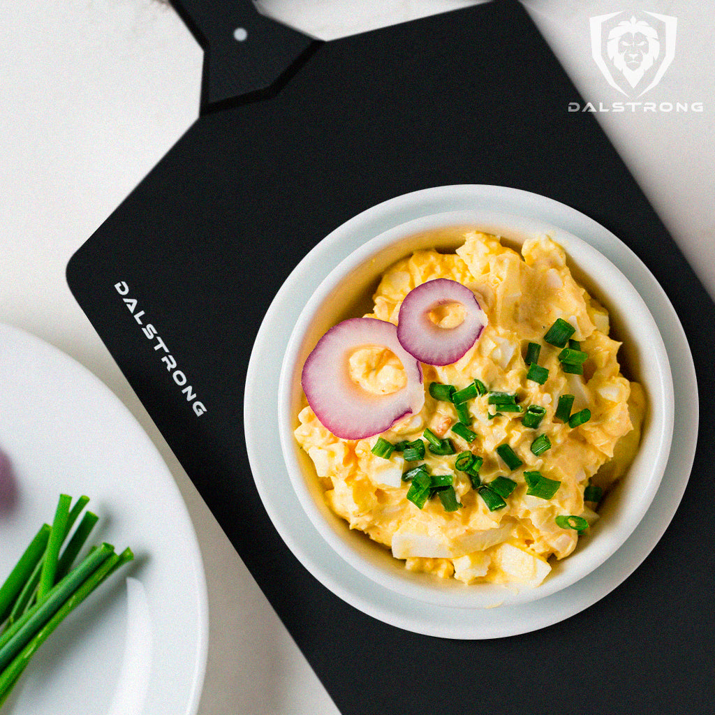 White bowl full of creamy egg salad on a black Dalstrong Black Cutting Board