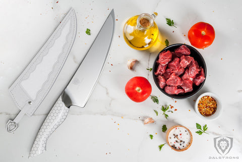 Chef knife with white handle on white marble next to small cups of sauces and diced meat