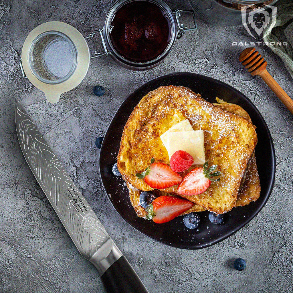 A stunning steak knife beside a delicious french toast topped with strawberries and blueberries