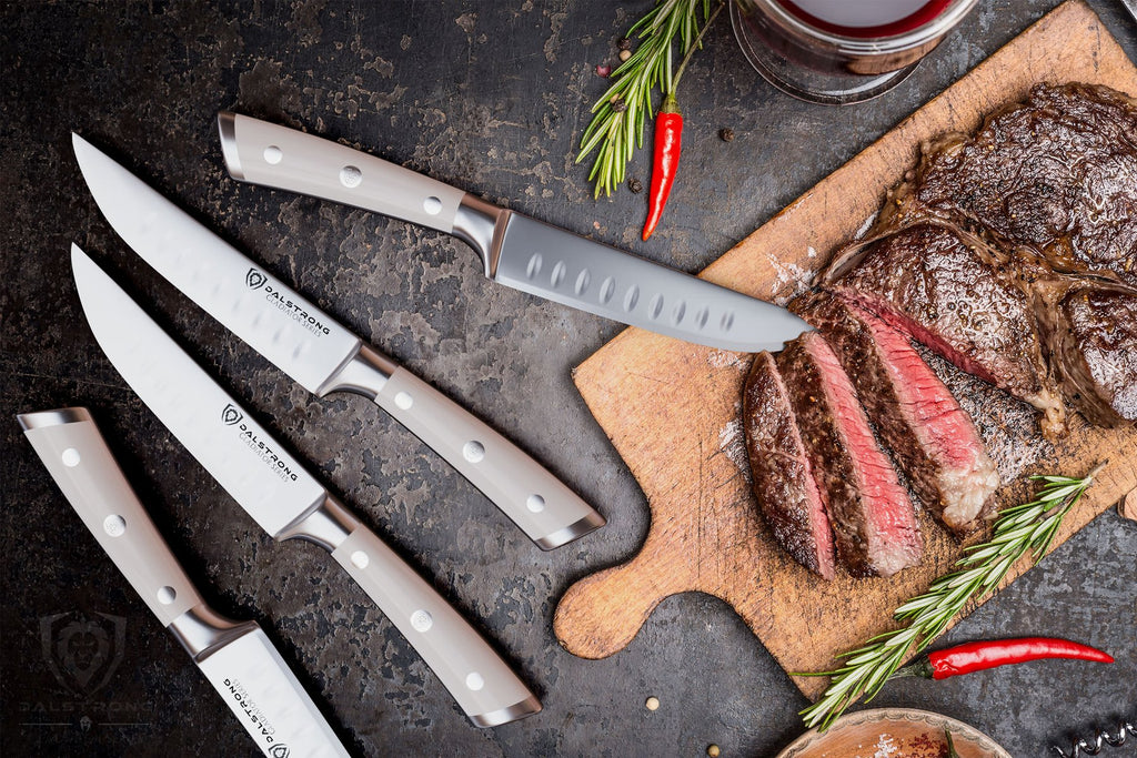 Four steak knives with white handles next to sliced cooked steak on a wooden cutting board