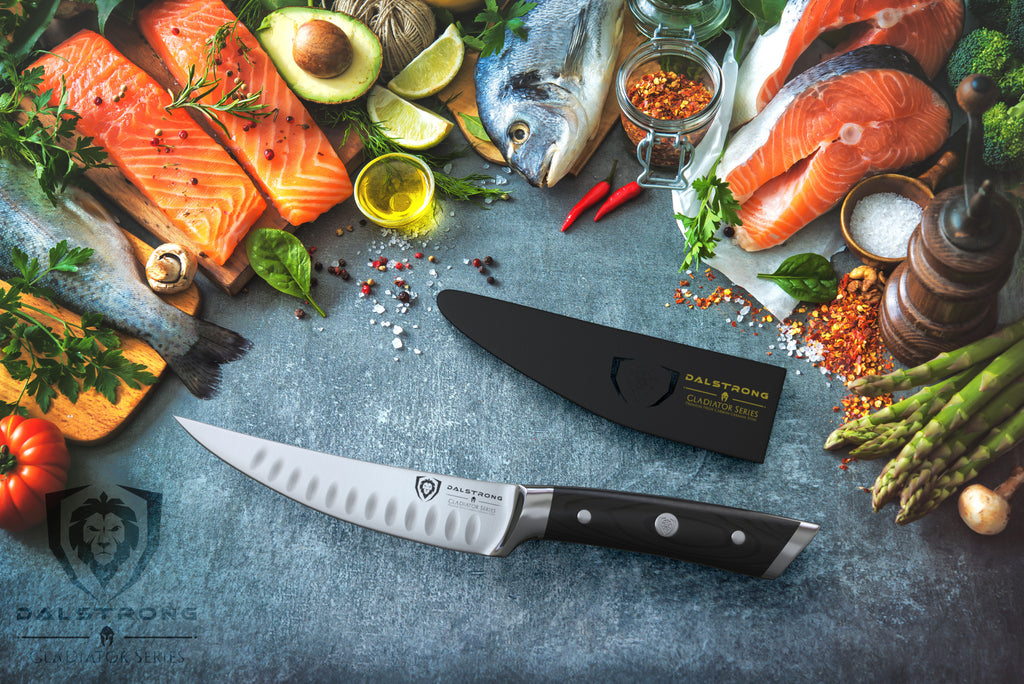 Fillet knife and sheath surrounded by uncooked fish and vegetables on a blue surface